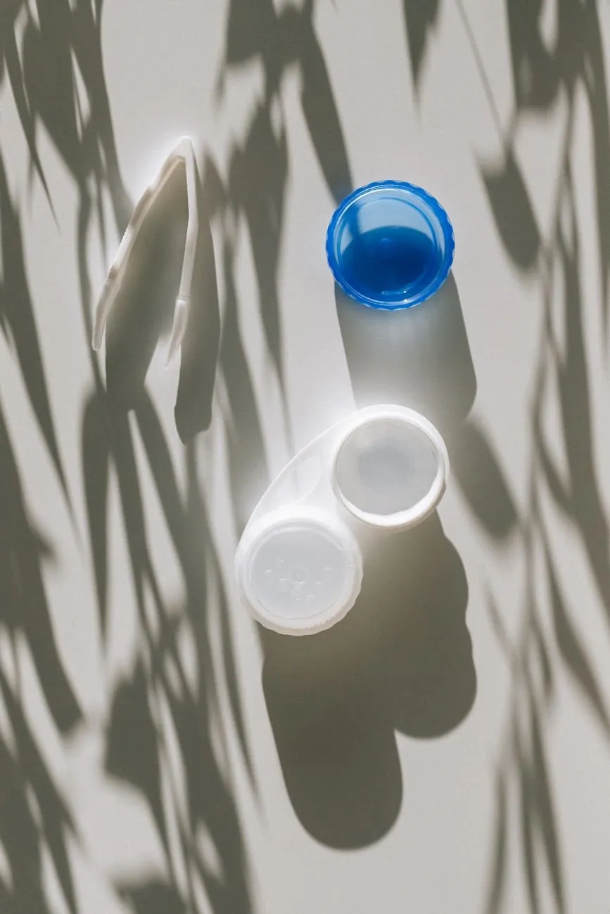 An open contact lens case on a white surface with leaf shadows