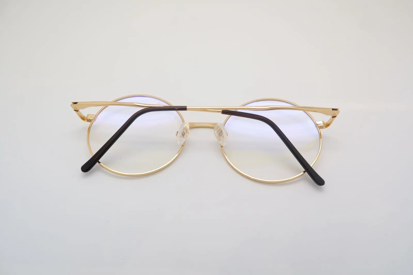 Round gold metal glasses with a straight brow bar on a white surface