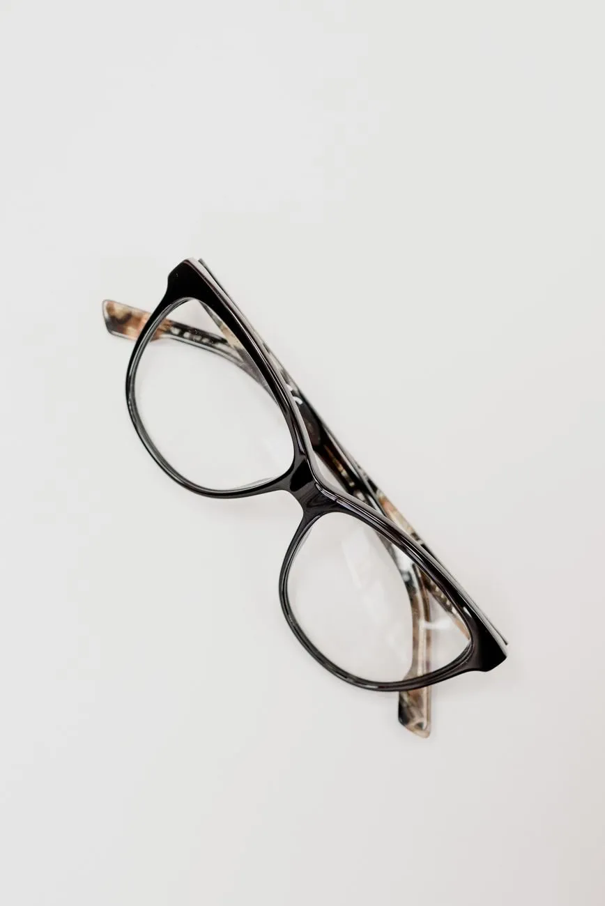 Black cat-eye glasses with tortoiseshell arms folded on a white surface