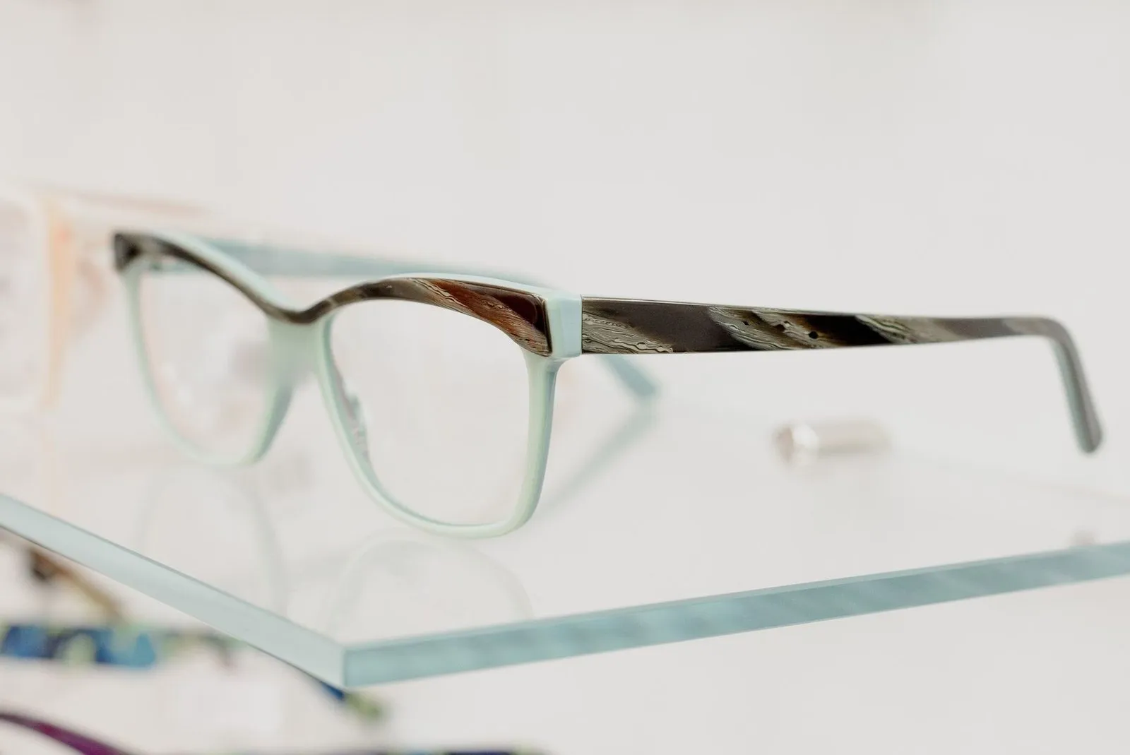 Mint cat-eye glasses with horn-patterned arms on a glass shelf