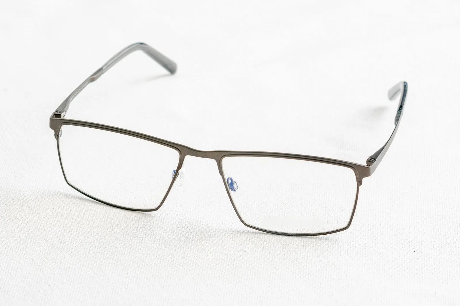 Gunmetal titanium rectangular glasses on a white textured surface