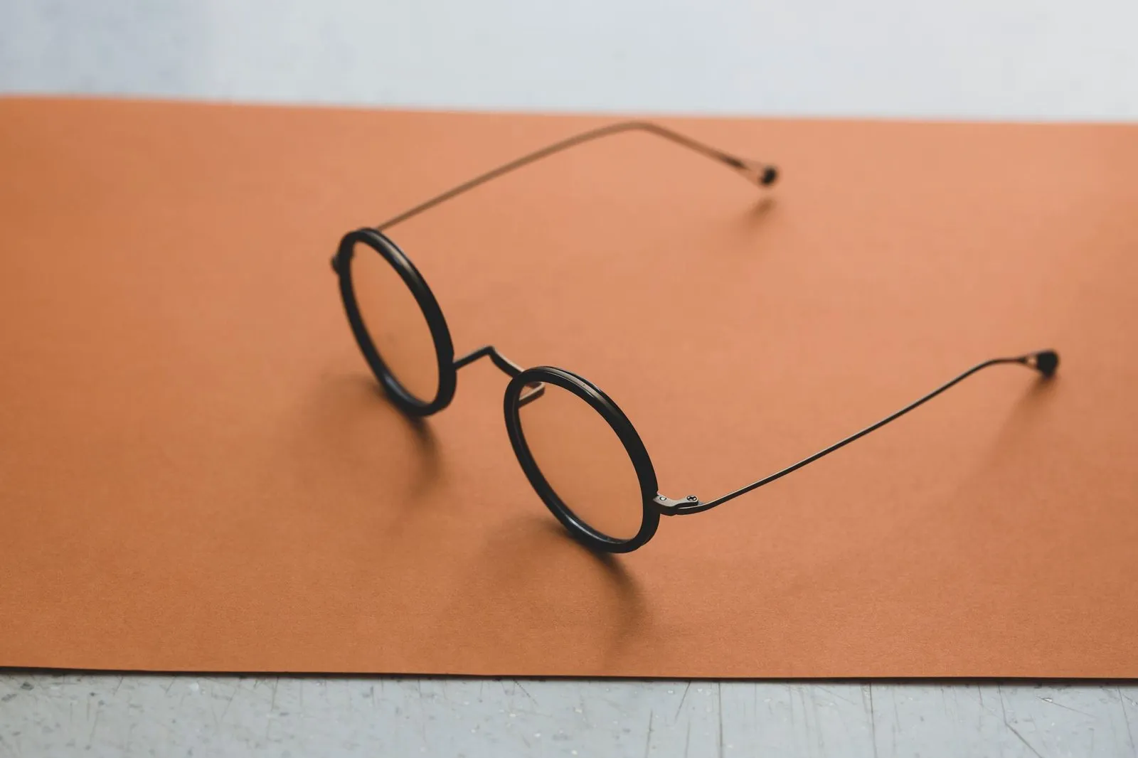 Thin black round glasses with fine titanium arms on terracotta card