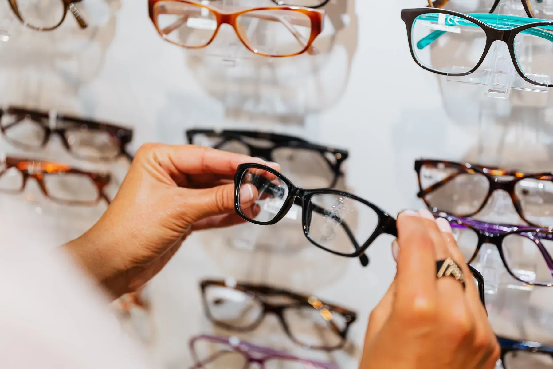 Two hands comparing a pair of frames at the dispensing rack