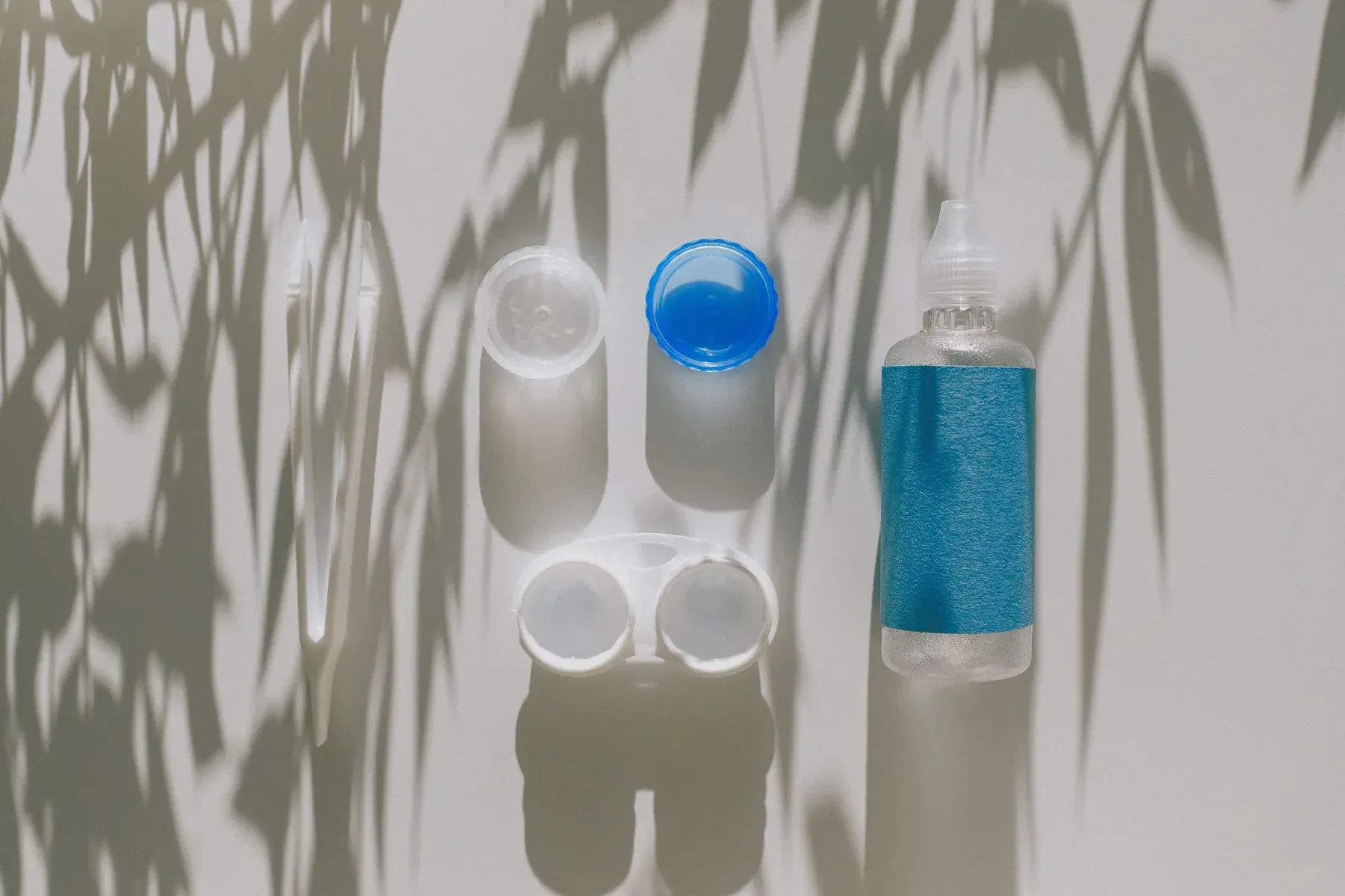 Contact lens cases and a bottle of saline on a pale surface